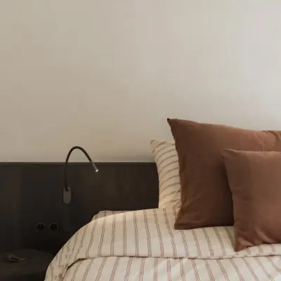 Bed met hoofdbord, leeslamp en terracotta kussens, Appartement in Nieuwpoort, interieur Laura Calleeuw