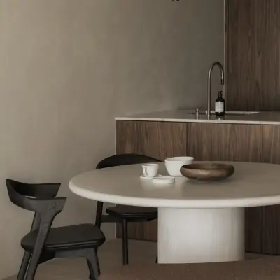Ronde eettafel met schalen en een zwarte stoel voor de houten keukenwand, Appartement in Nieuwpoort, interieur Laura Calleeuw