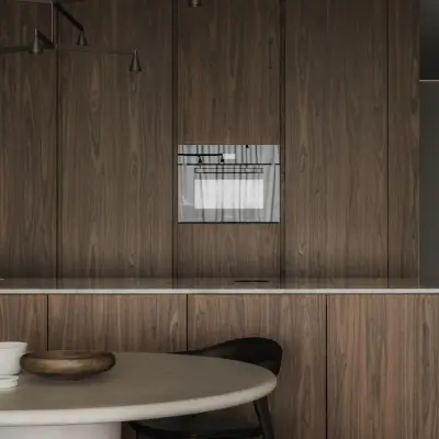 Houten keukenkasten met inbouwoven en een ronde eettafel op de voorgrond, Appartement in Nieuwpoort, interieur Laura Calleeuw