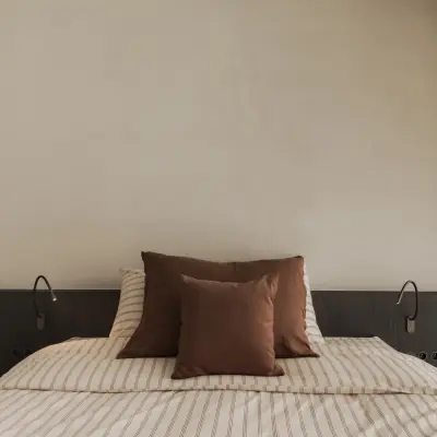 Slaapkamer met bed in gestreept beddengoed, terracotta kussens en donker hoofdbord, Appartement in Nieuwpoort, interieur Laura Calleeuw