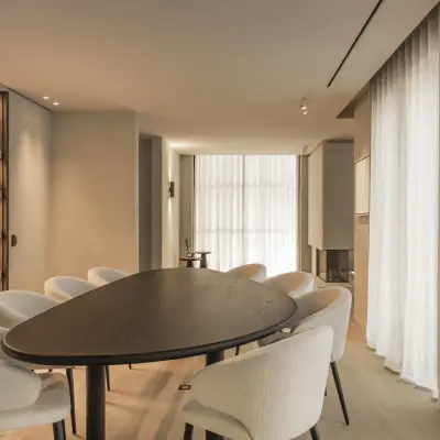 Eetkamer met ovale donkere tafel, ronde stoelen en een verlichte kast met ribbelwand, Gezinsvilla in Heusden-Zolder, interieur Laura Calleeuw