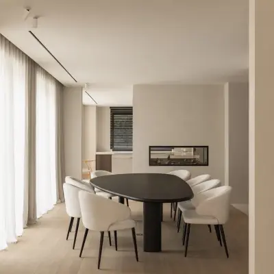 Eetkamer met ovale donkere tafel, ronde witte stoelen en een lage open haard, Gezinsvilla in Heusden-Zolder, interieur Laura Calleeuw