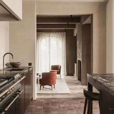 Doorkijk van de keuken naar de leefruimte met een roestkleurige fauteuil, Hoeve in Westkapelle, interieur Laura Calleeuw