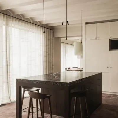 Keuken met kookeiland, barkrukken en lange gordijnen voor het raam onder gekalkte balken, Hoeve in Westkapelle, interieur Laura Calleeuw