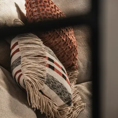 Detail van kussens met franjes en een patroon naast een zwart raamkader, Hoeve in Westkapelle, interieur Laura Calleeuw