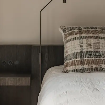 Bed met leeslamp en geruit sierkussen tegen donker eiken hoofdeinde, Schuur in Westkapelle, interieur Laura Calleeuw