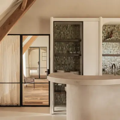 Golvend keukeneiland in microcement met verlichte voet en barkrukken, Schuur in Westkapelle, interieur Laura Calleeuw