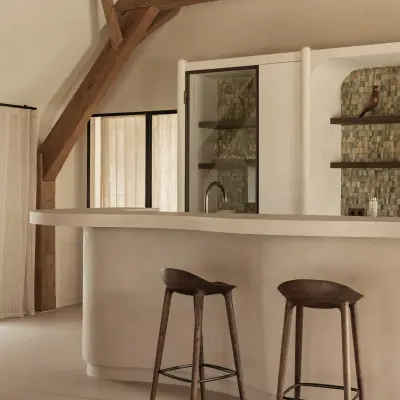 Golvend keukeneiland in microcement met verlichte voet en barkrukken, Schuur in Westkapelle, interieur Laura Calleeuw
