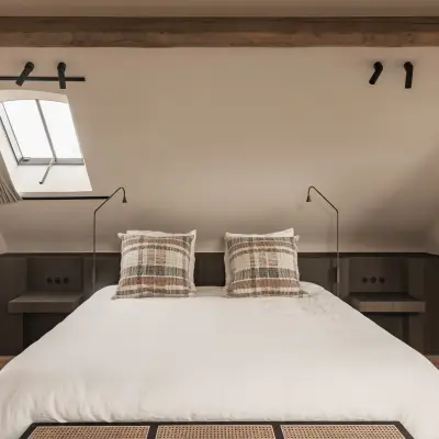 Slaapkamer onder het dak met bed, dakraam en geruite sierkussens, Schuur in Westkapelle, interieur Laura Calleeuw