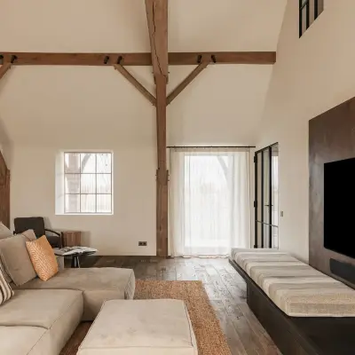 Woonkamer met televisiepaneel in roestkleurig metaal, hoekzetel en eikenhouten spanten, Schuur in Westkapelle, interieur Laura Calleeuw