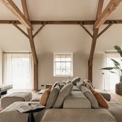 Woonkamer met televisiepaneel in roestkleurig metaal, hoekzetel en eikenhouten spanten, Schuur in Westkapelle, interieur Laura Calleeuw
