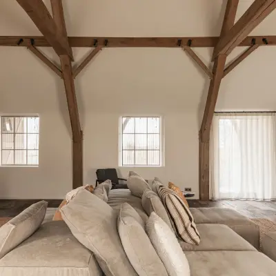 Woonkamer met televisiepaneel in roestkleurig metaal, hoekzetel en eikenhouten spanten, Schuur in Westkapelle, interieur Laura Calleeuw